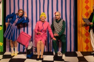 Szenenfoto: Frau Marthe sitzt neben Richter Adam. Sie hat ihre linke Hand auf seinem rechten Knie. Links steht Eve, sie lauscht. Schreiber Licht protokolliert.