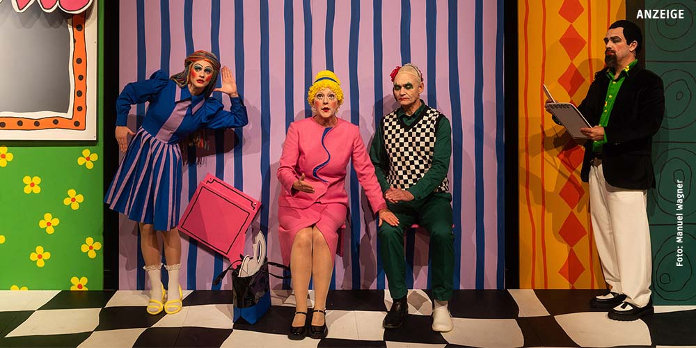 Szenenfoto: Frau Marthe sitzt neben Richter Adam. Sie hat ihre linke Hand auf seinem rechten Knie. Links steht Eve, sie lauscht. Schreiber Licht protokolliert.